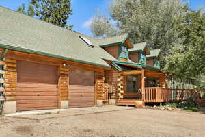 Log cabin with log exterior, a garage, a shingled roof, and driveway