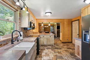 Kitchen featuring appliances with stainless steel finishes, wooden walls, a peninsula, light brown cabinetry, and light countertops