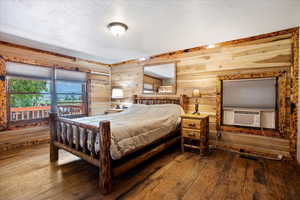 Bedroom with hardwood / wood-style floors, a textured ceiling, cooling unit, and wooden walls
