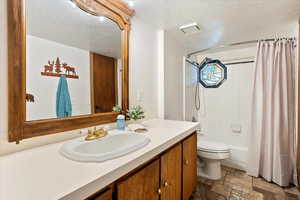 Full bath featuring stone tile flooring, a textured ceiling, vanity, and shower / bath combo with shower curtain