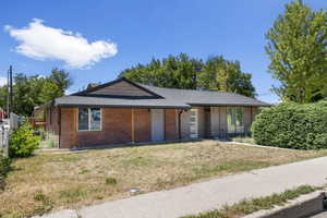 View of front of home with brick siding, roof with shingles, a chimney, and a front lawn