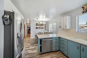 Kitchen with stainless steel appliances, a peninsula, light countertops, light wood-type flooring, and a chandelier