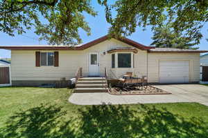 Ranch-style home featuring an attached garage, concrete driveway, a front yard, and a metal roof