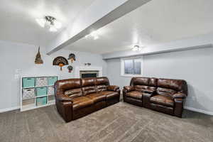 Living area with carpet floors, a textured ceiling, a fireplace, and beam ceiling