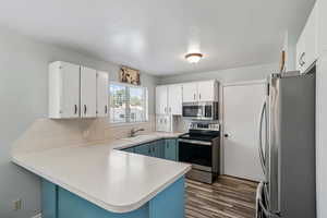 Kitchen featuring stainless steel appliances, a peninsula, dark wood-style floors, light countertops, and white cabinetry