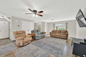 Living area featuring ceiling fan, wood finished floors, storage closet and door leading to unfinished basement
