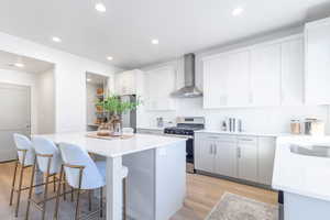 Kitchen with wall chimney range hood, appliances with stainless steel finishes, a kitchen island, a breakfast bar area, and light wood-type flooring