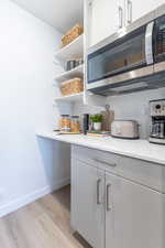 Kitchen featuring stainless steel microwave, open shelves, backsplash, light countertops, and light wood-style floors