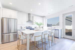 Kitchen with stainless steel appliances, wall chimney range hood, a center island, a kitchen bar, and light countertops