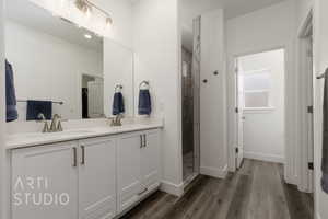 Full bath featuring double vanity, a tile shower, and wood finished floors