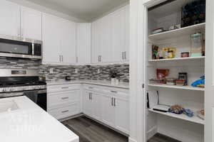 Kitchen with appliances with stainless steel finishes, dark wood finished floors, light countertops, and white cabinets