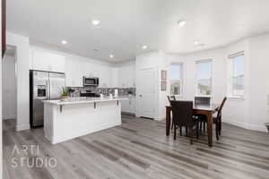 Kitchen featuring stainless steel appliances, light countertops, a breakfast bar area, white cabinets, and recessed lighting