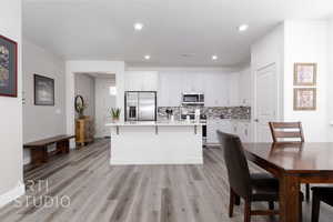 Kitchen with appliances with stainless steel finishes, white cabinets, backsplash, light countertops, and a kitchen island with sink