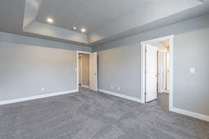 Unfurnished bedroom featuring a tray ceiling, dark carpet, and recessed lighting