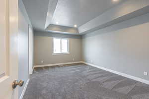 Spare room with a textured ceiling, dark carpet, a raised ceiling, and recessed lighting