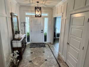 Foyer with inlaid floor details, a decorative wall, light tile patterned floors, and crown molding