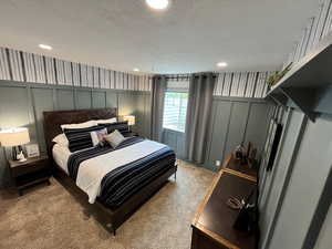 Bedroom with a decorative wall, light carpet, a textured ceiling, and recessed lighting