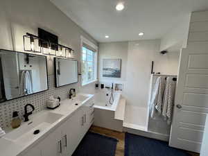 Full bathroom with wood finished floors, a whirlpool tub, double vanity, tasteful backsplash, and recessed lighting