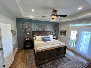 Bedroom with a tray ceiling, access to outside, light wood-style floors, and a ceiling fan