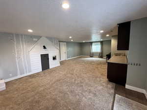 Below grade area featuring a textured ceiling, light carpet, recessed lighting, and a fireplace
