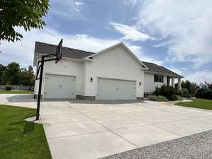 View of front facade with an attached garage, driveway, a shingled roof, and board and batten siding
