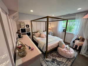Bedroom with a decorative wall, wood finished floors, and recessed lighting