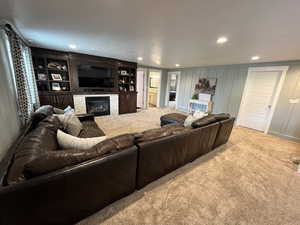 Living area with light colored carpet, recessed lighting, a glass covered fireplace, and a decorative wall