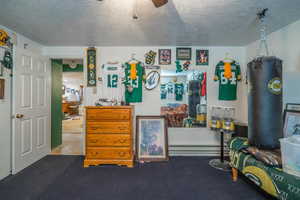 Carpeted bedroom featuring a baseboard heating unit, a textured ceiling, and a ceiling fan