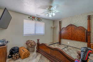 Bedroom with wood finished floors, a textured ceiling, ceiling fan, and wallpapered walls