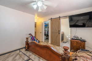 Bedroom with light wood-style flooring, a barn door, a walk in closet, a closet, and a textured ceiling