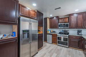 Kitchen featuring appliances with stainless steel finishes, light wood finished floors, light stone counters, dark brown cabinetry, and recessed lighting
