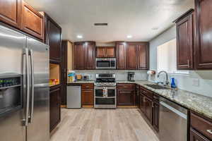 Kitchen featuring appliances with stainless steel finishes, light wood-style floors, light stone countertops, and dark brown cabinetry