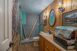 Bathroom with a textured ceiling, vanity, a shower, and wooden walls