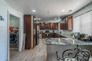 Kitchen with appliances with stainless steel finishes, washer / dryer, light wood finished floors, a peninsula, and a textured ceiling