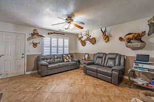 Living room with a ceiling fan, a textured ceiling, and light tile patterned floors