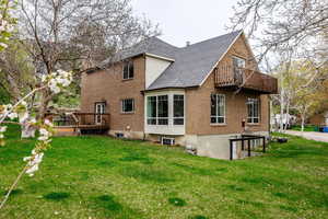 Rear view of property featuring a balcony, brick siding, a yard, a shingled roof, and a wooden deck