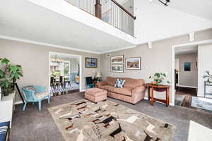 Living room with carpet floors, a chandelier, crown molding, and a high ceiling