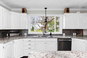 Kitchen with stainless steel dishwasher, light stone countertops, white cabinets, tasteful backsplash, and ornamental molding