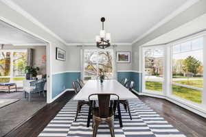 Dining area with plenty of natural light, a chandelier, dark wood-type flooring, and ornamental molding