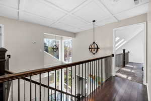 Hall featuring coffered ceiling, wood finished floors, a chandelier, beamed ceiling, and an upstairs landing
