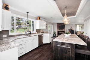 Kitchen with stainless steel dishwasher, dark wood-type flooring, tasteful backsplash, white cabinetry, and ornamental molding