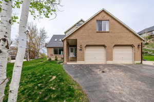 View of front of home with an attached garage, driveway, brick siding, and a front lawn