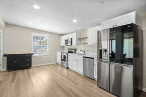 Kitchen featuring stainless steel appliances, white cabinetry, light wood-style floors, light countertops, and recessed lighting