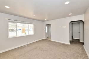 Carpeted empty room featuring arched walkways and recessed lighting