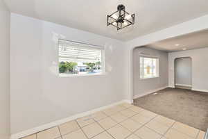 Unfurnished room featuring arched walkways, a chandelier, light colored carpet, light tile patterned floors, and recessed lighting