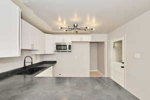 Kitchen featuring stainless steel microwave, dark countertops, white cabinets, light tile patterned flooring, and a chandelier