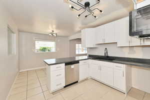 Kitchen with appliances with stainless steel finishes, a chandelier, light tile patterned floors, dark countertops, and white cabinetry