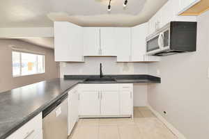 Kitchen with appliances with stainless steel finishes, white cabinets, dark countertops, and light tile patterned floors