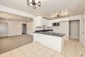 Kitchen with arched walkways, stainless steel microwave, dark countertops, light tile patterned flooring, and recessed lighting