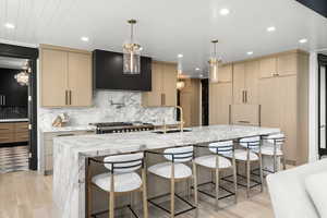 Kitchen with exhaust hood, light wood-type flooring, light brown cabinets, light stone counters, and recessed lighting